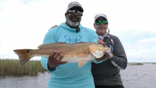 Two fishermen on a boat with one holding a large redfish